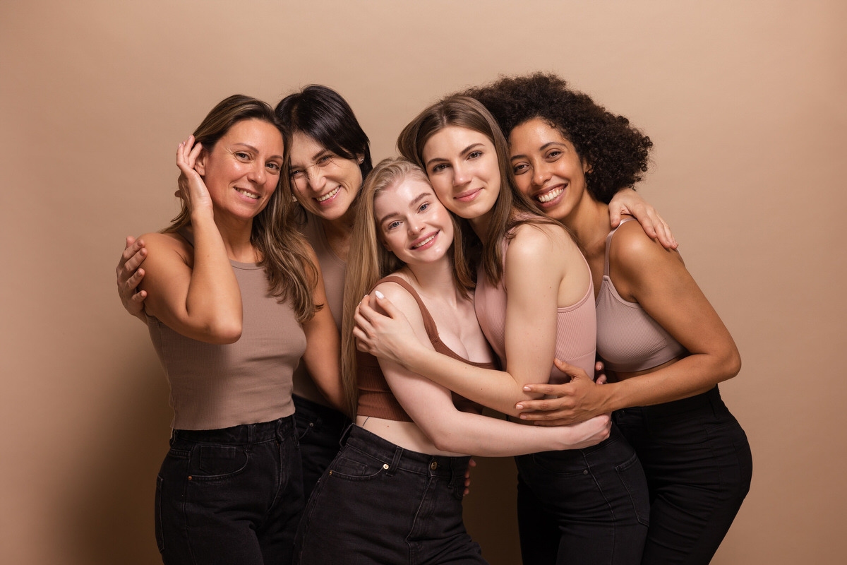 five-pretty-african-caucasian-women-brown-tops-black-jeans-look-camera-beige-background_1 five-pretty-african-caucasian-women-brown-tops-black-jeans-look-camera-beige-background_1